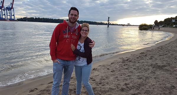 man and woman standing on the beach, posing for a picture