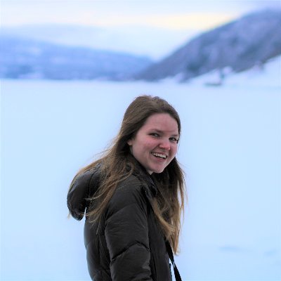 Woman with blonde/brown hair standing in the snow surrounded by mountains