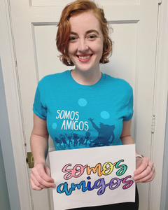 a woman with short hair holding up a sign that is written in Spanish, wearing a blue t-shirt