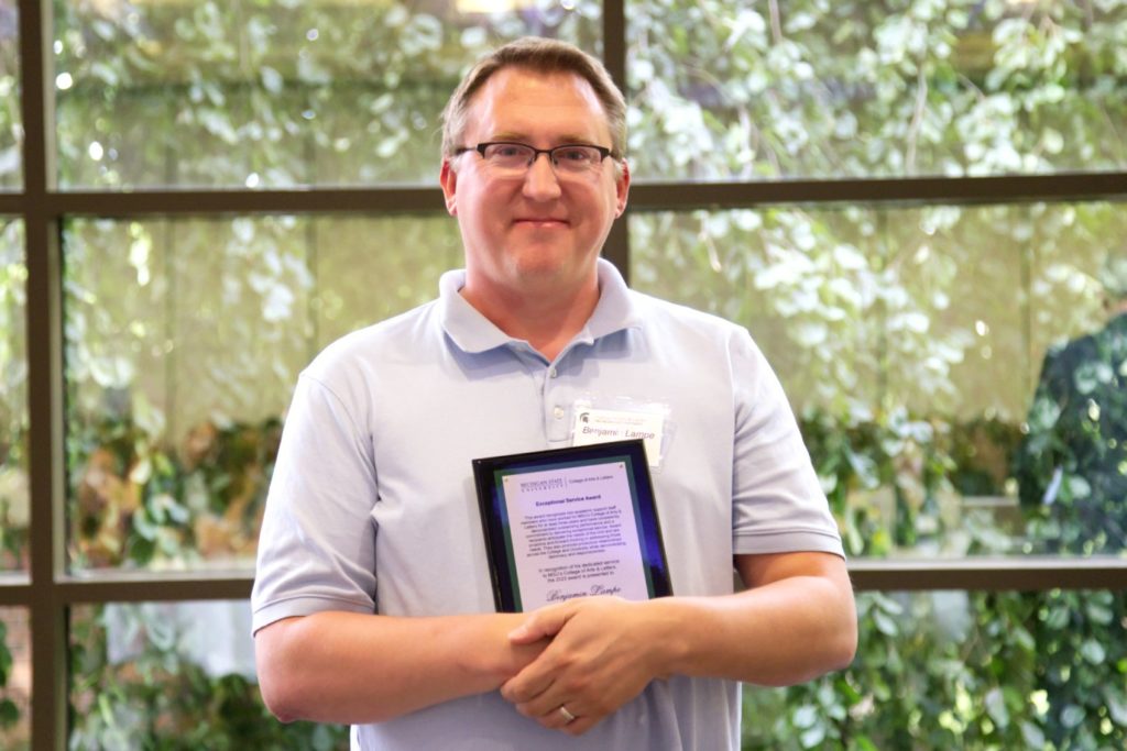 Man wearing a light blue short-sleeved shirt holding a plaque.