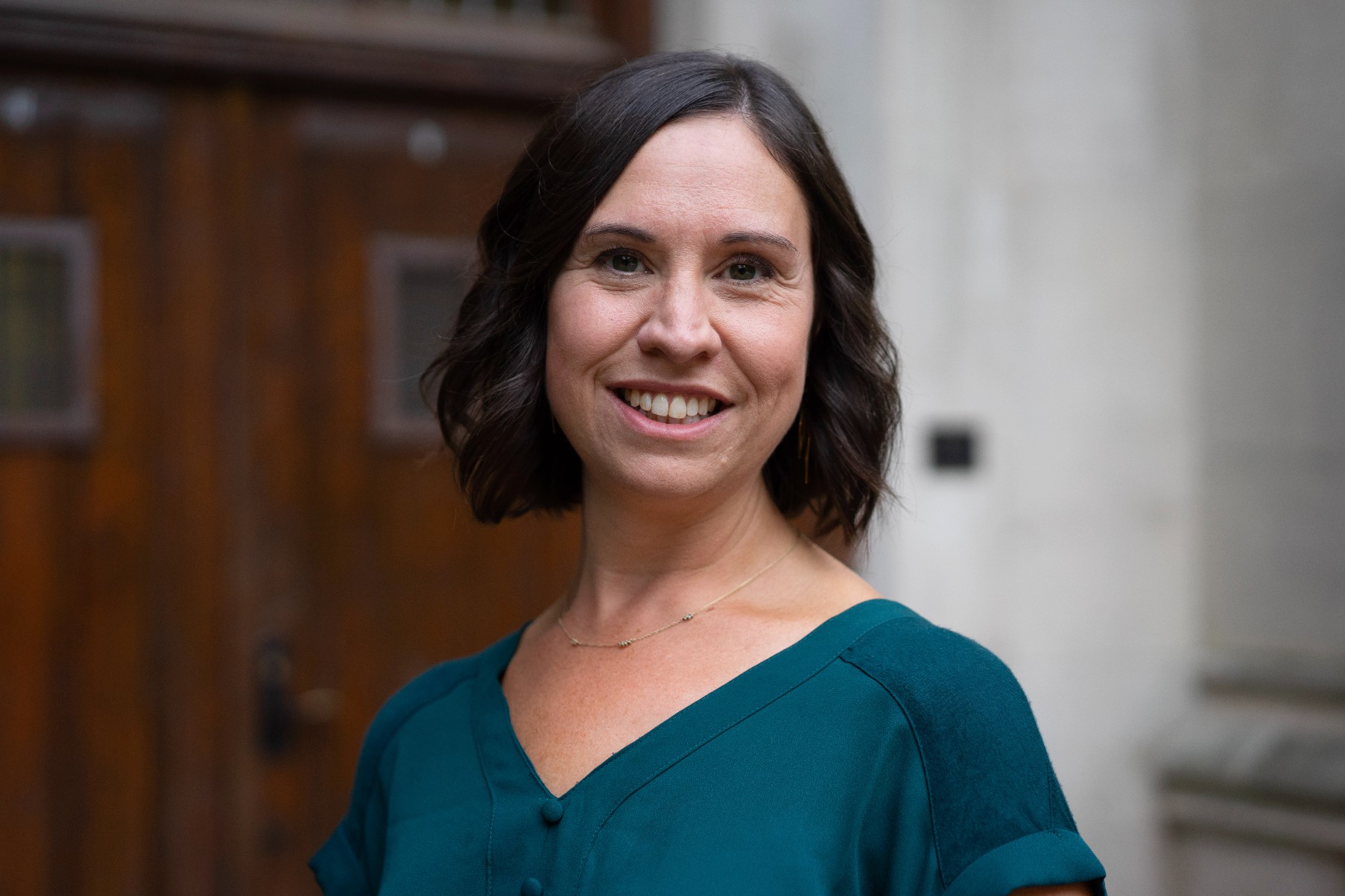 A picture of a woman with a blue shirt in front of a brown door and white wall. 