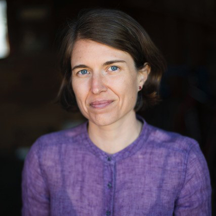 A picture of a woman with a purple blouse in front of a dark background. 