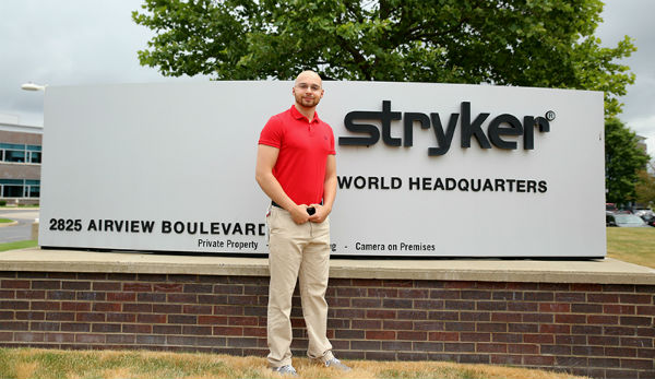man in a red polo standing in front of stryker world headquarters sign