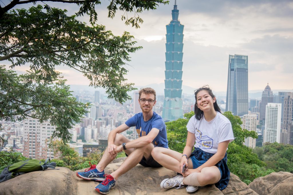 man and woman sitting on a rock outlooking a city