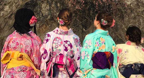 four girls facing away from the camera in brightly colored kimonos covered in flower patterns
