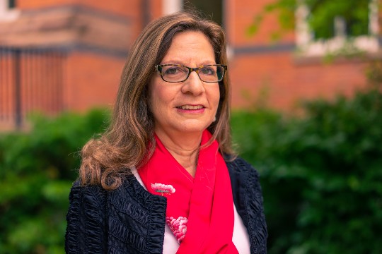 headshot of a woman with long brown hair wearing glasses a black blazer and a red scarf