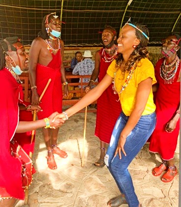 A woman wearing a yellow t-shirt and jeans shakes hands with another person wearing a traditional red garment.