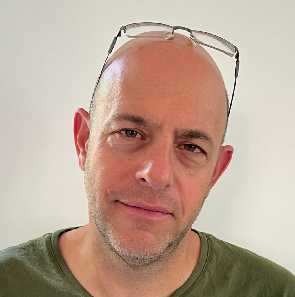 Portrait of a bald man with eyeglasses on his head wearing a green shirt.