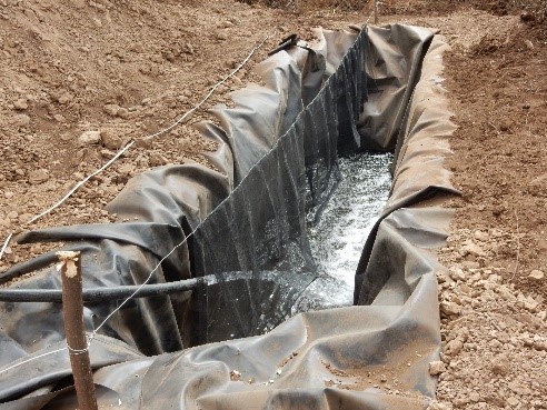 Picture of a long pit with tarp being filled with water