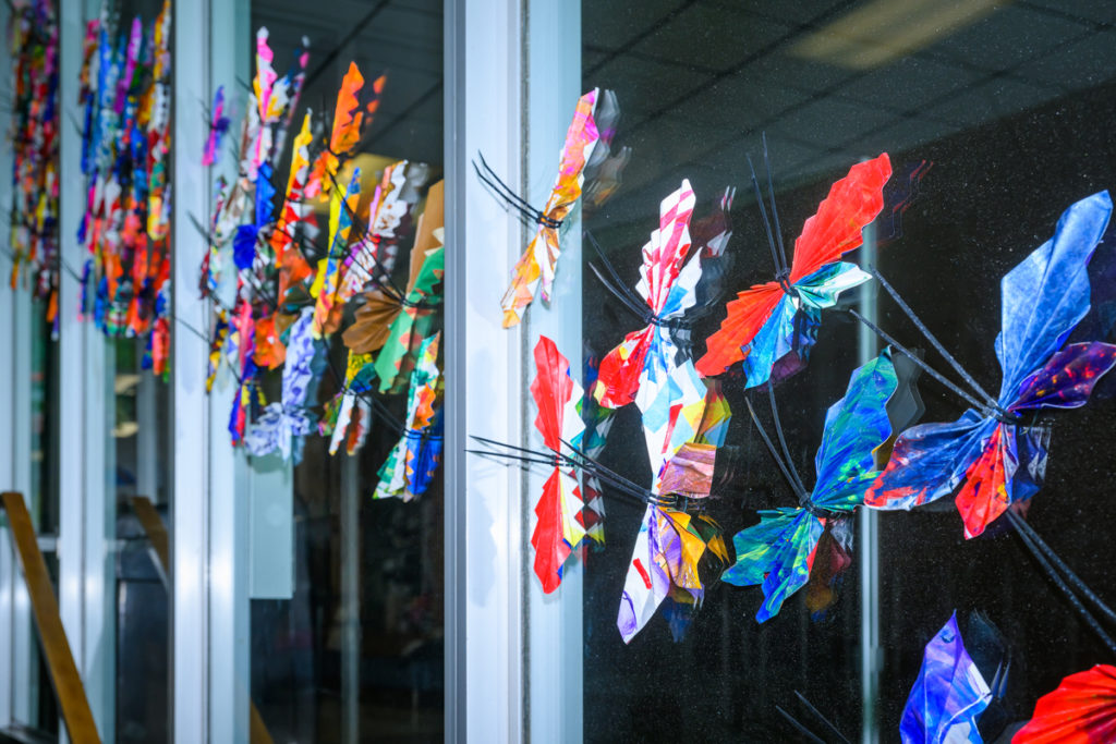 A close up of a colorful array of paper butterflies placed along a glass window. 