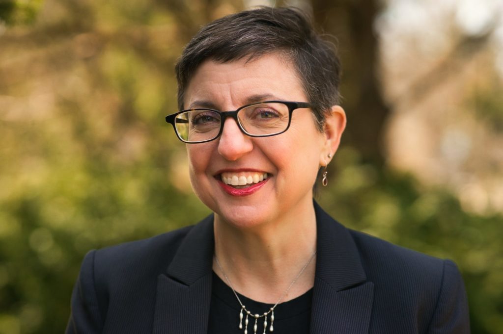 A picture of a woman with short hair and glasses wearing a black blazer. 