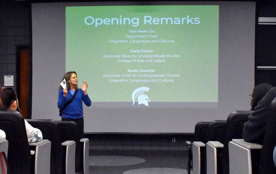 Photo os a woman standing in front of an audience and in front of a screen that says "Opening Remarks"