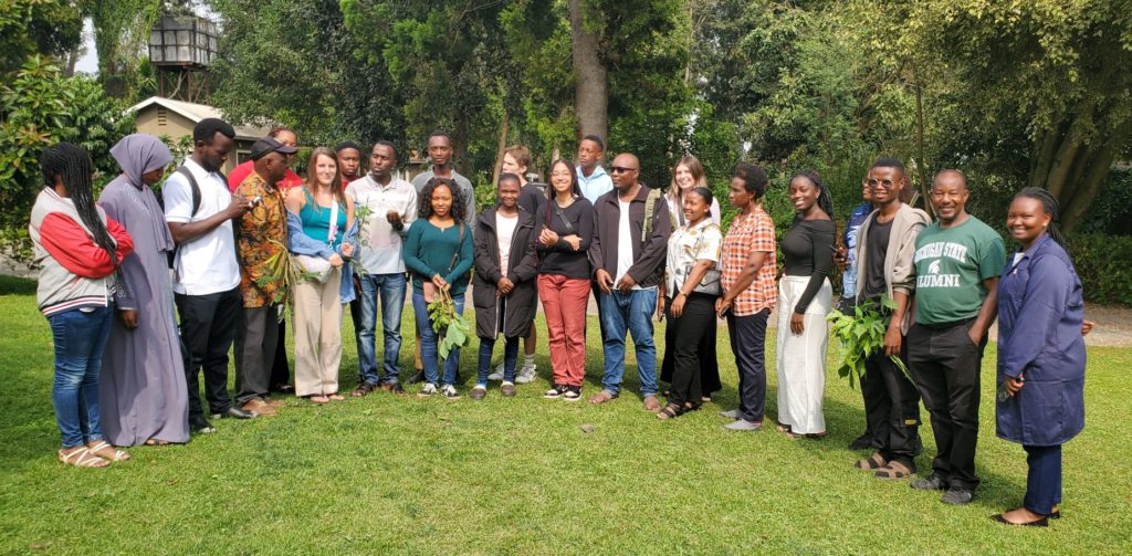 a group photo of 23 people who are standing outside in a semi circle. 