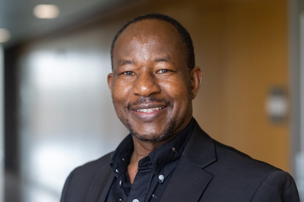 black man who is smiling and wearing a black suit.