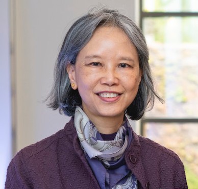 Headshot photo of an Asian woman who is smiling and has short gray hair and is wearing a purple jacket and scarf. 