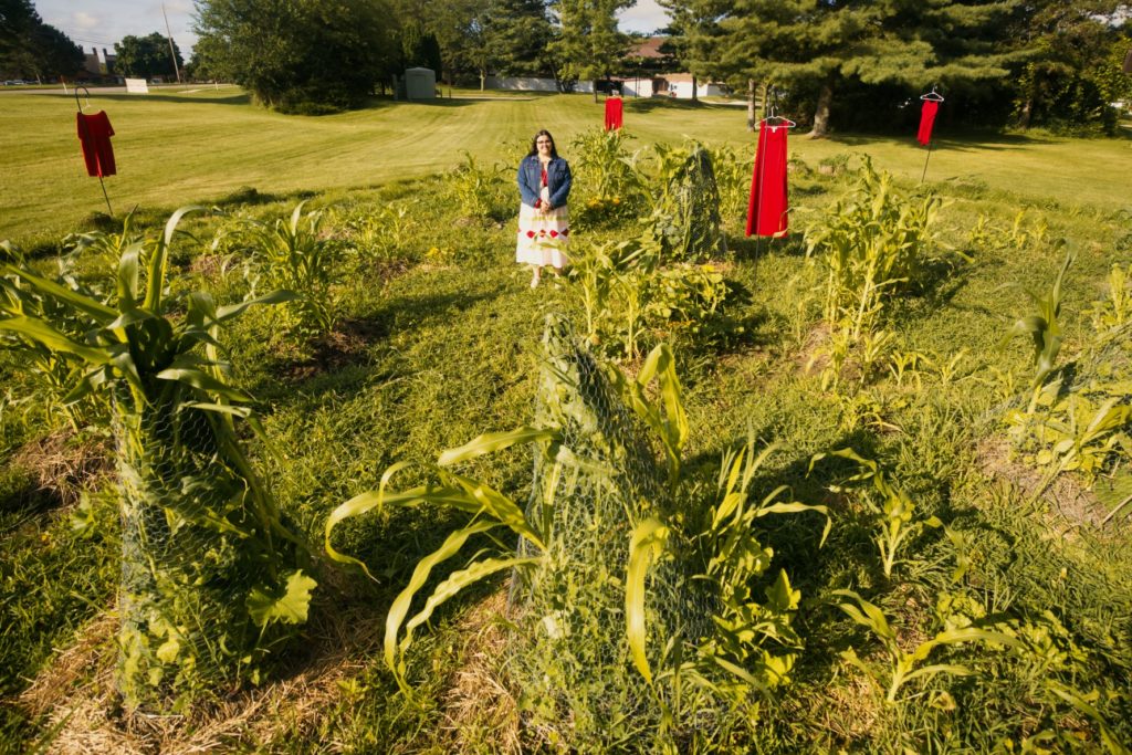 A picture of a person in a jean jacket and a white and red dress standing in a green garden